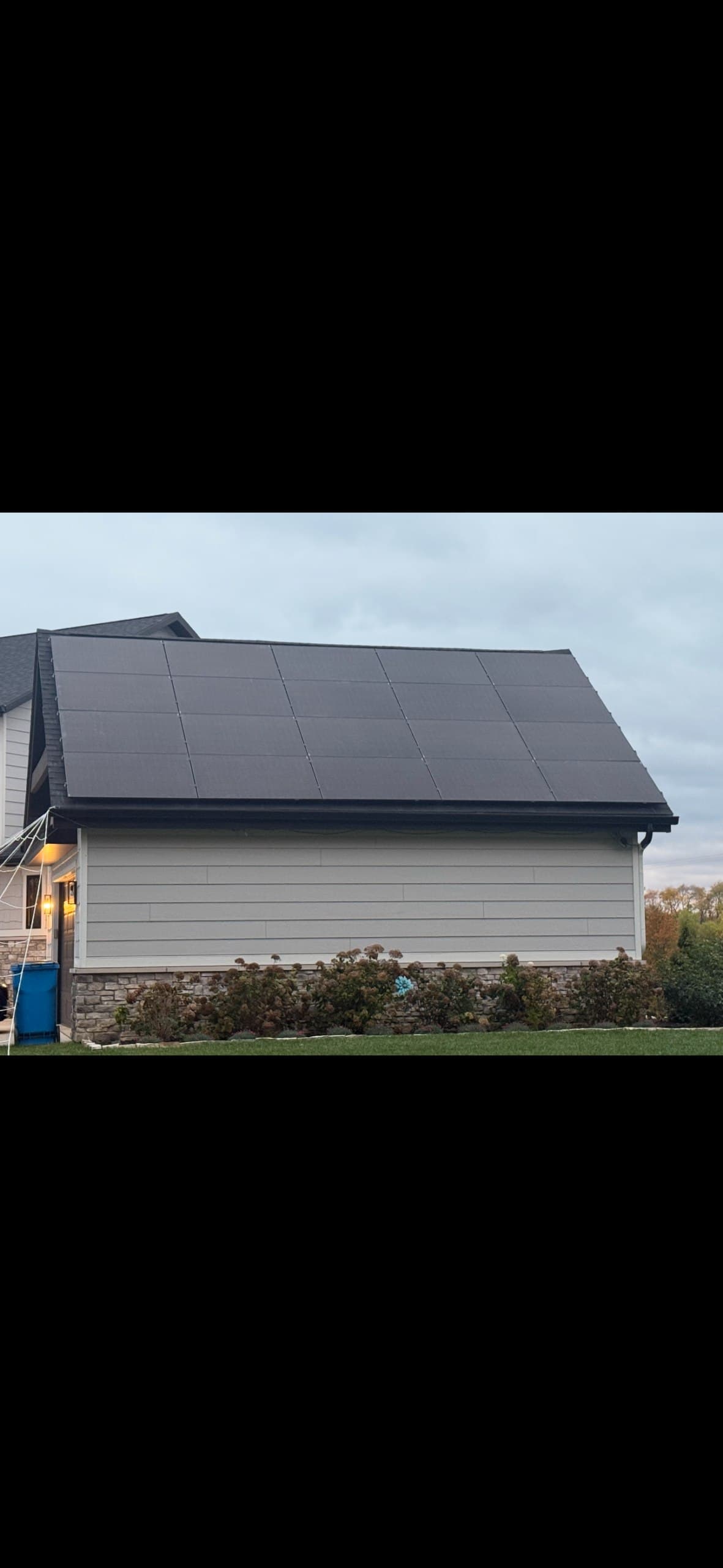 Solar panels covering the garage roof of a home with stone accents and green lawn