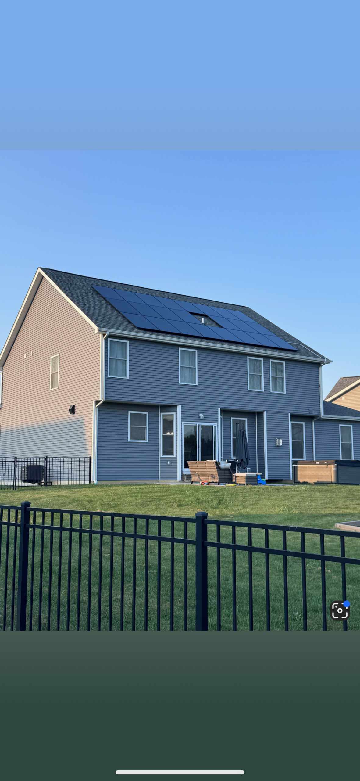 Blue-sided two-story home with solar panels on the back roof and fenced yard