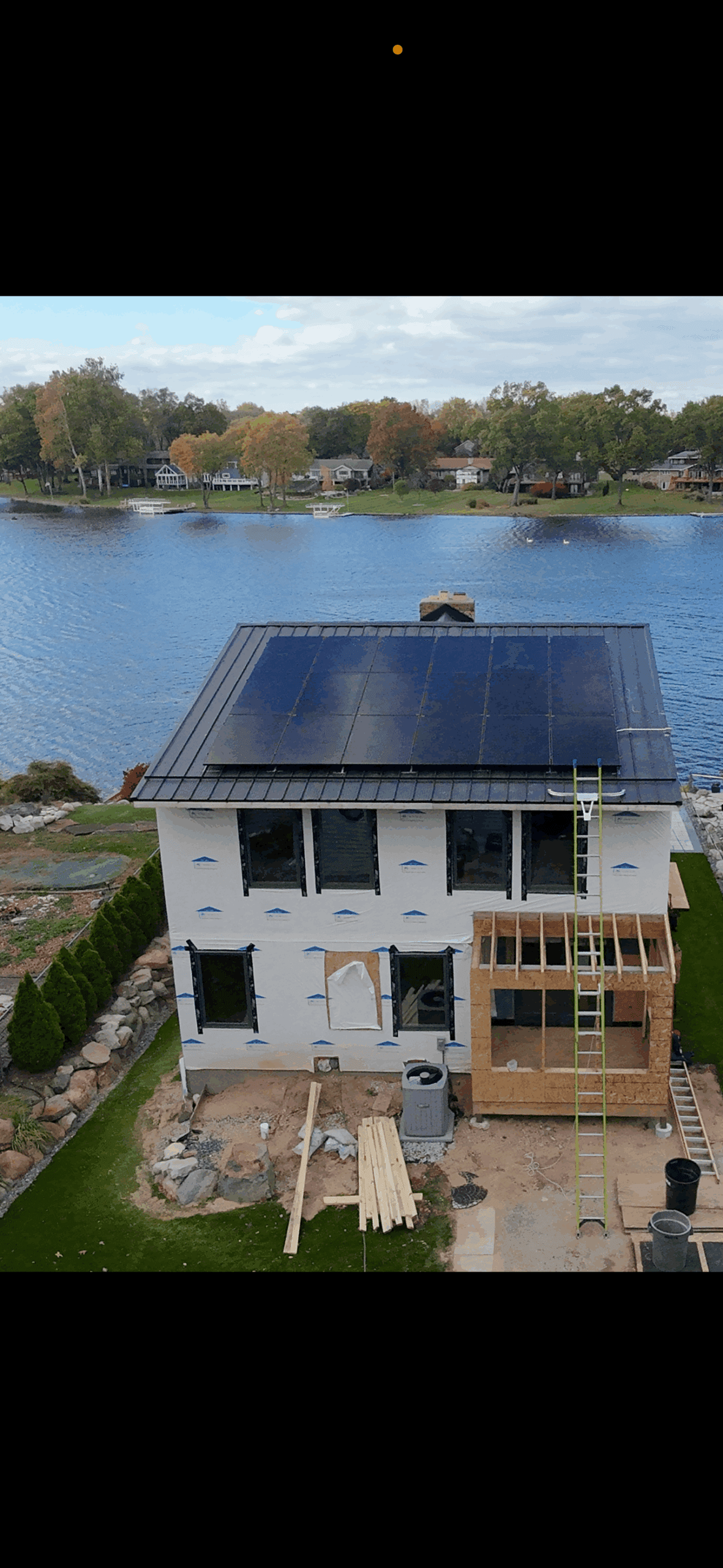 Aerial view of lakefront home with full solar panel coverage on roof